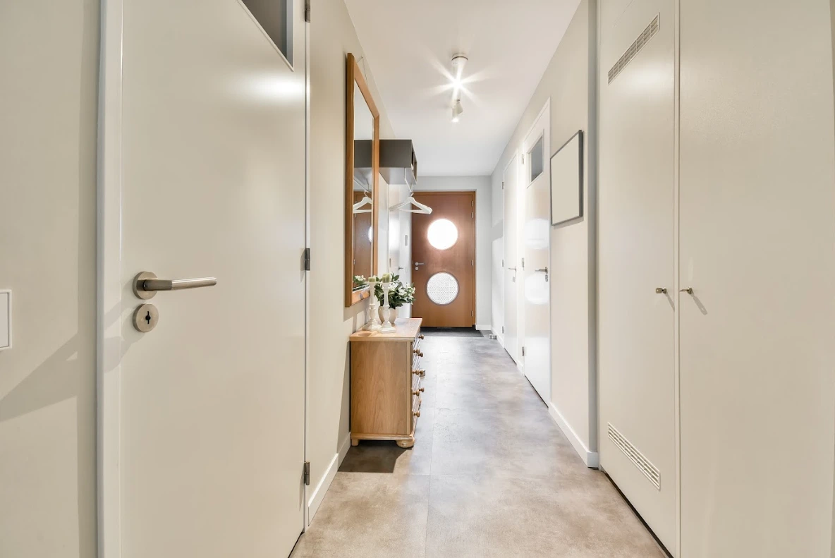 Modern hall med ljusa väggar, trägolv och stilren inredning.